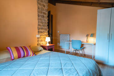 Dieses gemütliche Schlafzimmer verfügt über ein Bett mit einer blauen Bettdecke, bunten Kissen, einer Akzentwand aus Stein, einem Schreibtisch, einem Stuhl, einem Kleiderschrank und einer warmen Raumbeleuchtung.