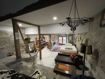 This cozy room features stone walls, rustic wooden beams, a chandelier, bookshelves, a bed, a couch, a coffee table, and large glass doors for light.