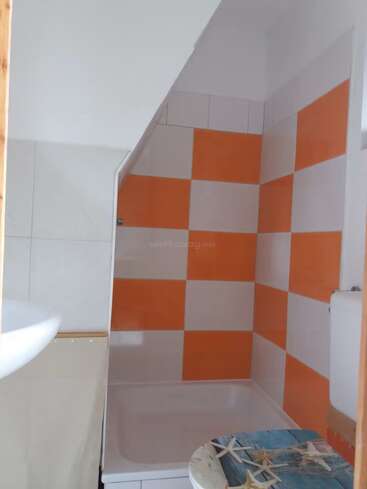Das Bild zeigt ein kleines Badezimmer mit einer Dusche, die mit orange-weiß karierten Fliesen ausgelegt ist. Der Toilettensitz hat ein Seestern-Design.