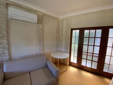 Esta acogedora habitación cuenta con un pequeño sofá gris, una mesa redonda, aire acondicionado, paredes de ladrillo blanco y puertas francesas de madera con cristales esmerilados.