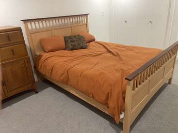 Une chambre confortable avec un lit en bois recouvert d'une couette orange, de deux oreillers orange et d'un coussin à motifs. Une commode en bois se trouve à côté du lit.
