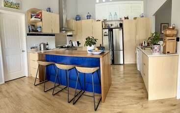 The image depicts a modern kitchen with a large island, featuring a sink and stove, accompanied by a dining table and chairs, set against a neutral-colored background. The overall atmosphere is clean and organized.