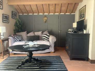 Un acogedor salón muestra un sofá en tonos pastel con cojines a rayas, una mesa de centro negra, una alfombra a rayas, paredes con paneles oscuros, un techo inclinado de madera y varios adornos en la pared.