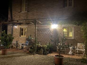 Un acogedor patio de ladrillo por la noche, cálidamente iluminado, con bancos, macetas, estatuas de jardín, enrejado de madera y un encanto rústico que crea un ambiente exterior tranquilo y acogedor.