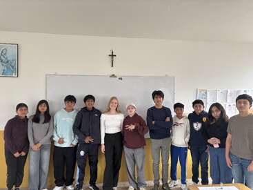 Un grupo de doce alumnos está de pie frente a una pizarra blanca en un aula, sonriendo. En la pared que tienen detrás cuelgan un crucifijo y unas obras de arte.