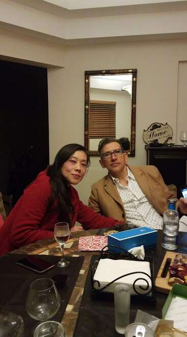 Un hombre y una mujer sentados en una mesa de comedor con vasos, aperitivos y servilletas, posan juntos en el interior de una acogedora casa con espejo.