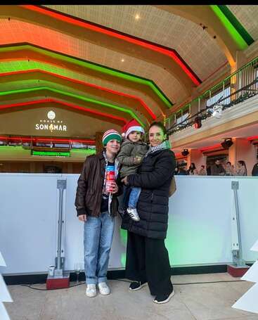 A woman and two children, wearing festive hats and winter clothes, pose indoors under colorful red and green lights at a venue labeled "House of Sonmar."