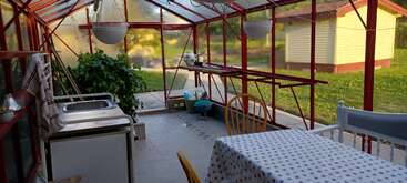 Cette image montre une serre confortable avec un encadrement rouge, une nappe à pois sur une table à manger, un petit évier de cuisine, des plantes vertes et un paysage extérieur.