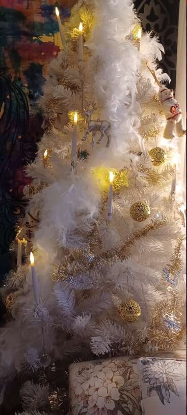 Un sapin de Noël blanc décoré d'ornements dorés, de bougies, de guirlandes blanches duveteuses, de rennes étincelants et d'ornements en forme d'ours festifs, créant une atmosphère de fête chaleureuse.