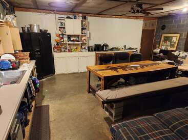 Dieses Bild zeigt eine rustikale Küche und einen Essbereich mit Betonböden, offenen Regalen, einem langen Holztisch, gepolsterten Bänken, Geräten und einer eklektischen, gemütlichen Einrichtung.