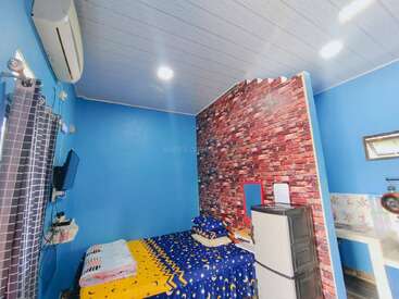 This cozy room features bright blue walls, a faux brick accent wall, star-patterned bedding, air conditioning, TV, dresser, small desk, and neatly stacked towels for guests.
