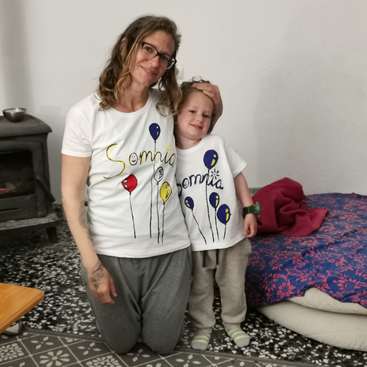 Das Bild zeigt eine Frau und ein Kind, die für ein Foto posieren. Beide tragen passende weiße T-Shirts mit dem Wort "Somnia" und Luftballonmotiven.