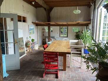 Este acogedor solárium cuenta con una mesa de comedor de madera, sillas de colores, plantas de interior, suelo de ladrillo, grandes ventanales y vigas rústicas, que crean un ambiente cálido y acogedor con luz natural.