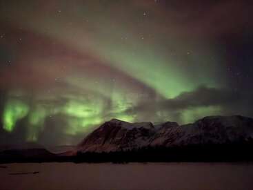 Un fascinante espectáculo de auroras boreales verdes baila en el cielo nocturno sobre las montañas cubiertas de nieve, con las estrellas titilando en el oscuro y sereno paisaje invernal.