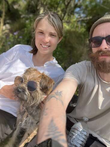 Une femme, un homme et un chien portant des lunettes de soleil profitent d'une journée ensoleillée à l'extérieur. Ils ont l'air heureux et détendus, et prennent un selfie tous ensemble.