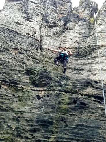 A person wearing a harness climbs a steep, rugged rock face. Ropes for safety are visible, highlighting an adventurous outdoor rock climbing activity in nature.