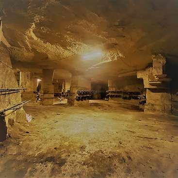 The image depicts a dimly lit, dusty underground room with a rough concrete floor and walls, featuring a central light source and various objects on the walls.