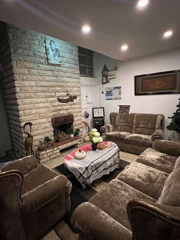 Dieses gemütliche Wohnzimmer ist mit braunen Samtsofas, einem gemauerten Kamin, einem Couchtisch mit Blumen, Kunstwerken an den Wänden und warmen, sanften Deckenleuchten ausgestattet.