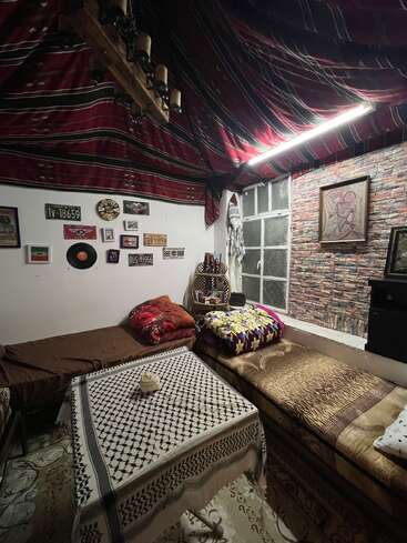 Ein gemütliches, vielseitiges Zimmer mit einer gestreiften Stoffdecke, zwei Betten, einem gemusterten Tisch, Ziegelstein-Tapete, Vintage-Dekor, Nummernschildern, Wandbildern und warmer Stimmungsbeleuchtung.