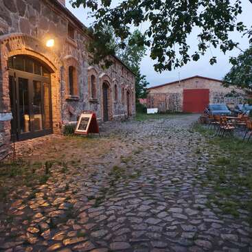 La imagen muestra un sereno edificio de piedra con ventanas arqueadas, un camino empedrado y una puerta de garaje roja, rodeado de frondosos árboles y un ambiente tranquilo.