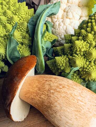 Cette image montre un gros plan de légumes frais : un gros cèpe, un brocoli romanesco vert aux motifs fractals et un chou-fleur blanc.