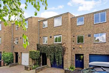 This image shows a row of modern, three-story brick townhouses with large windows, blue doors, garages, and some greenery, including ivy climbing the central facade.