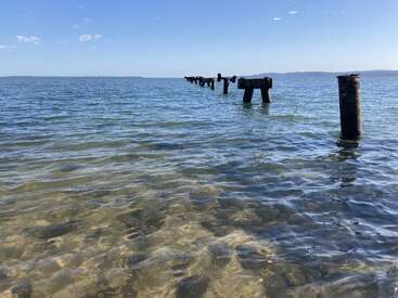 L'eau bleue claire s'étend vers l'horizon. Des piliers cassés émergent de la mer. Une terre lointaine et un ciel bleu avec quelques nuages complètent la scène.