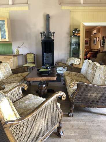 Dieses gemütliche Wohnzimmer ist mit Holzmöbeln im Vintage-Stil, einem zentralen Couchtisch, verzierten Sofas, einem Holzofen, gelb-grünen Akzenten und charmanten rustikalen Dekorationselementen ausgestattet.