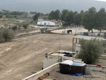 Cette scène rurale montre une cour clôturée, un couple de chevaux, des arbres épars, des bâtiments blancs, un jacuzzi et des montagnes en arrière-plan. Atmosphère paisible.