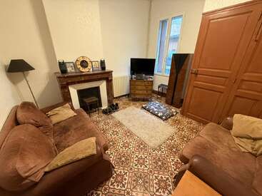 Dieses gemütliche Wohnzimmer verfügt über braune Sofas, gemusterte Fliesen, einen Kamin, einen Fernseher, Holzmöbel, einen großen Schrank, Kissen, eine Lampe und ein Fenster, das für natürliches Licht sorgt.