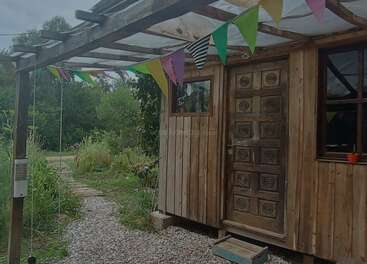 A rustic wooden cabin with a uniquely carved door stands among greenery. Colorful triangular pennant banners decorate the porch, inviting a cheerful, welcoming atmosphere outdoors.