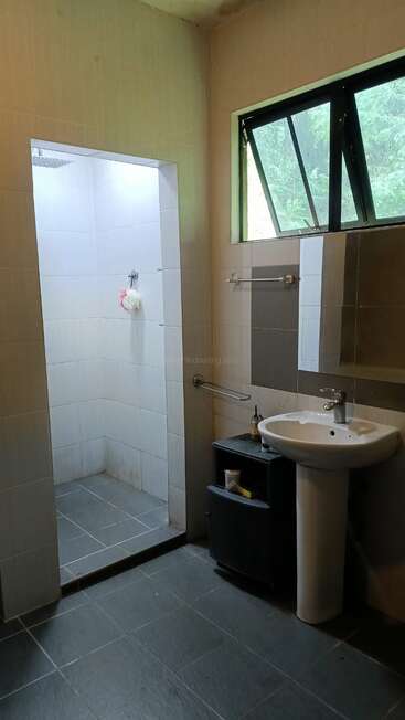 This image shows a modern bathroom with a tiled shower area, a pedestal sink, a wall mirror, a small storage cabinet, and a large open window.