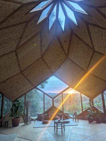 Dieser gemütliche, geometrisch gestaltete Holzraum hat große Fenster mit toller Aussicht auf die Berge, durch die sanftes Sonnenlicht hereinscheint, Zimmerpflanzen, Bodenkissen und eine ruhige, entspannte Atmosphäre.