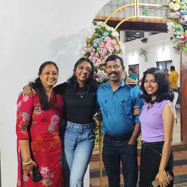 Cuatro personas sonríen y posan juntas delante de un arco floral. Parecen felices y festivos, probablemente en una celebración o evento especial en el interior.