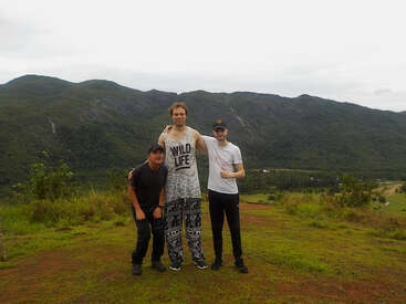 Drei Männer posieren zusammen auf einem grasbewachsenen Hügel mit üppig grünen Bergen im Hintergrund. Sie wirken glücklich und genießen die Natur und die schöne Landschaft, die sie umgibt.