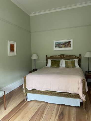 The image depicts a serene bedroom with sage green walls, a gold-framed bed, and a light wood floor, exuding a sense of calm and tranquility.