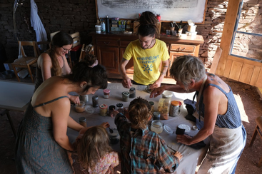 Eine Gruppe von Erwachsenen und Kindern sitzt in einem sonnigen Raum um einen Tisch herum und macht eine kreative, praktische Aktivität mit Gläsern. Sie haben Spaß daran, gemeinsam was zu lernen.