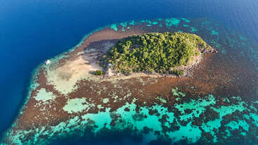 A imagem retrata uma ilha tropical serena com uma pequena península, com um corpo de água tranquilo e vegetação exuberante, evocando uma sensação de relaxamento e beleza natural.