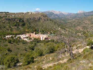 The image depicts a serene mountainous landscape with a large building in the distance, surrounded by lush greenery and a clear blue sky.