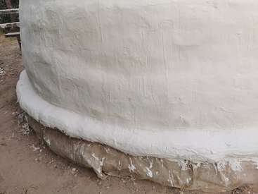 The image depicts a large, white, textured structure with a rounded base, situated on a dirt surface, likely under construction or renovation.