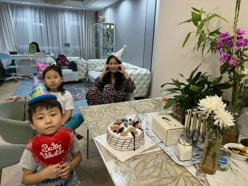 Eine Familie feiert zu Hause einen Geburtstag. Drei Personen tragen Partyhüte, auf dem Tisch steht eine Torte, und Blumen schmücken den hellen, gemütlichen Raum.