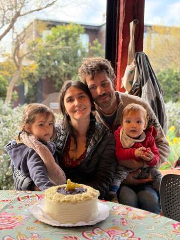 Une famille de quatre personnes est assise, souriant chaleureusement à l'appareil photo. Devant eux se trouve un gâteau d'anniversaire avec une bougie numéro 4, créant une atmosphère chaleureuse.