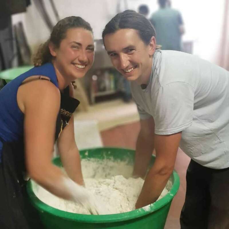 Deux personnes souriantes mélangent joyeusement de la pâte dans un grand récipient vert. Elles semblent faire de la pâtisserie ensemble dans un cadre intérieur confortable, en profitant de l'activité.