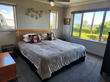 Um quarto aconchegante com uma cama grande, almofadas florais e roupa de cama macia. Janelas grandes oferecem vistas panorâmicas e muita luz natural. Decoração simples e moderna em todo o quarto.