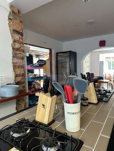 This image shows a modern kitchen with gas stovetops, utensil holders, knife blocks, plates stacked near exposed brick, and a well-lit, inviting open-plan layout.