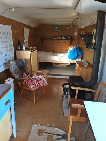 Cette cabane confortable et compacte dispose d'un lit simple, d'un poêle à bois, de murs en bois, de meubles simples, d'un petit coin cuisine, d'affiches et d'un décor rustique et pratique.