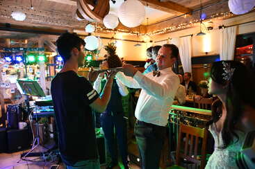 Scène de fête animée en intérieur avec des personnes participant à une activité amusante. Des lumières colorées, des décorations festives et des expressions joyeuses créent une atmosphère chaleureuse et festive.