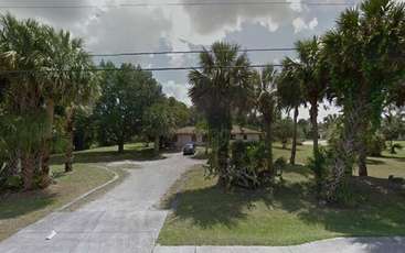 The image depicts a serene residential area with a row of houses, featuring a large yard with trees and a driveway, surrounded by a fence, evoking a sense of tranquility and suburban charm.
