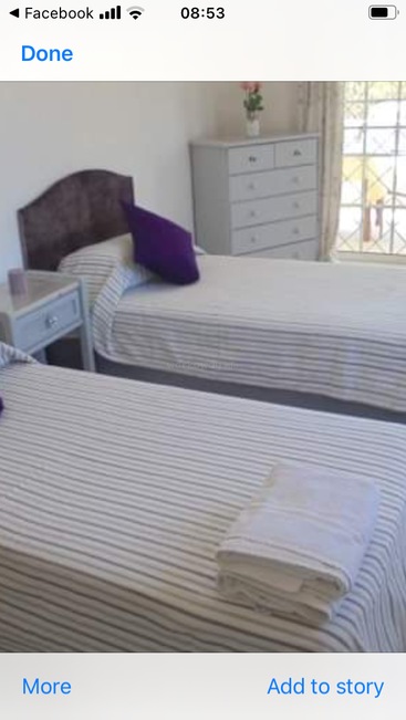 L'image représente une chambre à coucher sereine avec deux lits, chacun orné de draps rayés blancs et gris, une table de nuit et une commode, le tout posé sur un mur blanc impeccable.