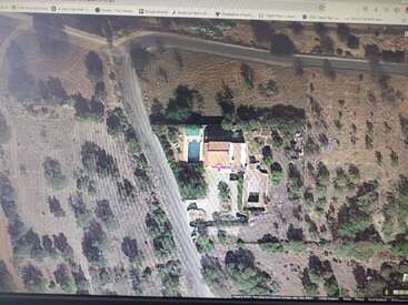 L'image montre une capture d'écran de Google Maps d'une zone rurale avec une maison, une piscine et une allée, entourée d'arbres et de champs, avec une route qui la longe.